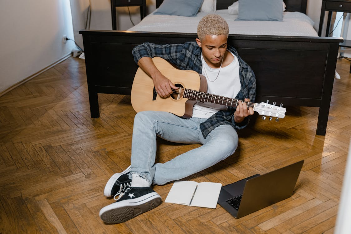 beginner using how to teach yourself a skill while practicing guitar at home with a laptop