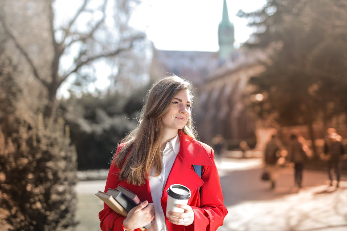 student trying to balance school work and life while carrying books and coffee outdoors