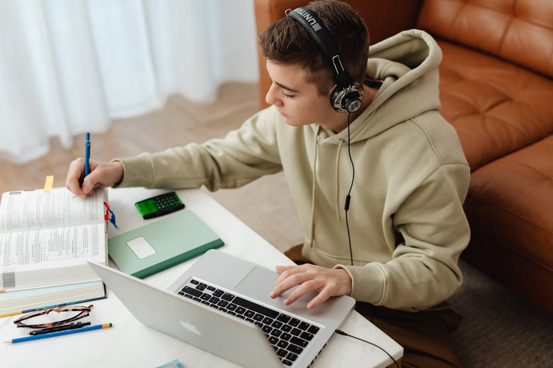 student multitasking while studying with laptop, headphones, and notebook at desk